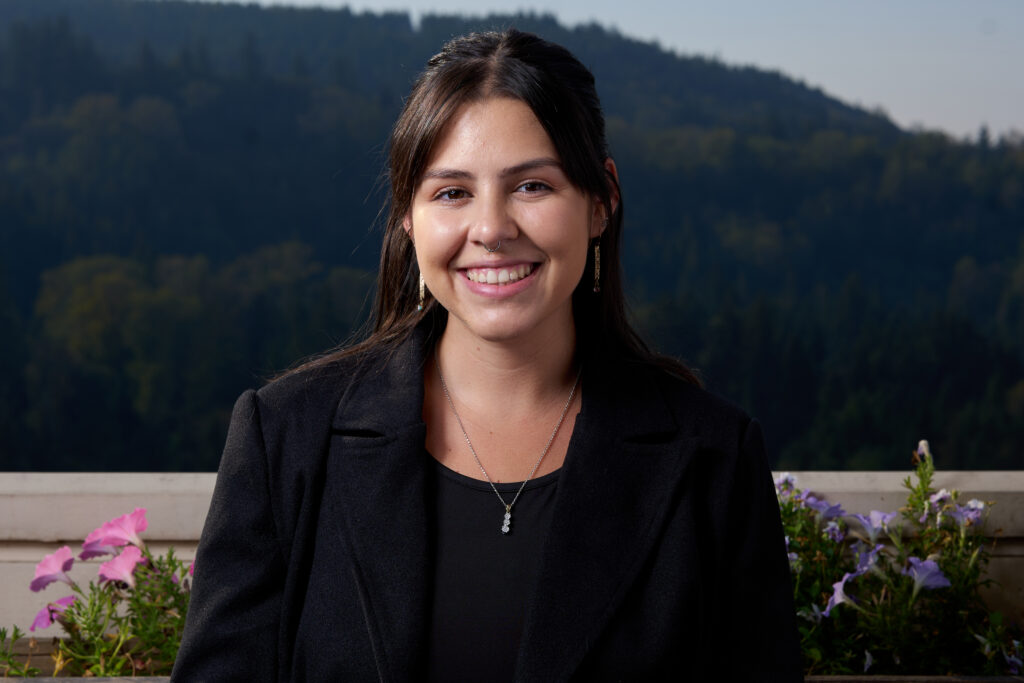 Sandy, wearing a black blazer and smiling in front of a blurred hillside. 