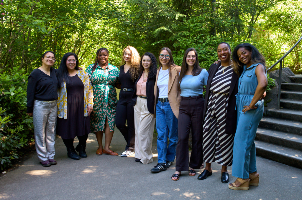 Pathwaves staff and Fellows stand embracing in front of a background of green trees and concrete steps. From left to right: Nubia, Sharissa, Maya, Samantha, Fernanda, Lish, Sandy, Shaterra, LaToya