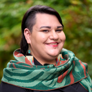 Barbara smiles in front of a green background wearing a green and burnt orange scarf