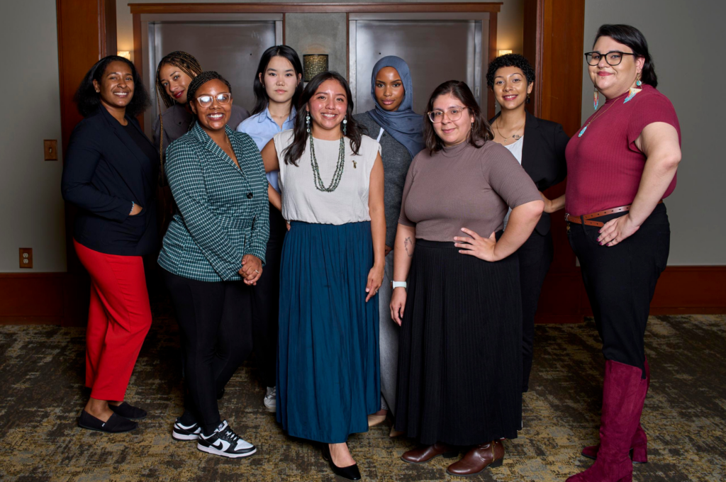 Nine leaders of color stand together, looking at the camera. Some are smiling, some have their hands on their hips with looks of determination