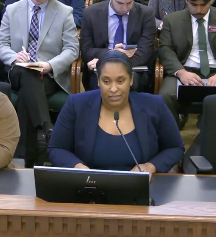 Raishawn giving her testimony for HB 2438. She is wearing a blue blazer and speaking into the microphone in front of a crowded room