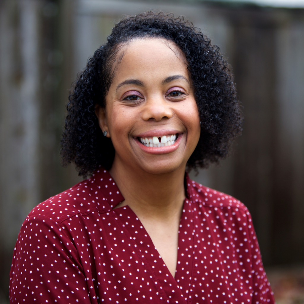 Brianna smiles wearing a maroon top. Her hair is curly and worn down.