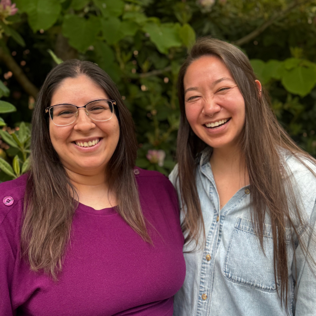 Dania and Lish stand smiling in front of a green bush